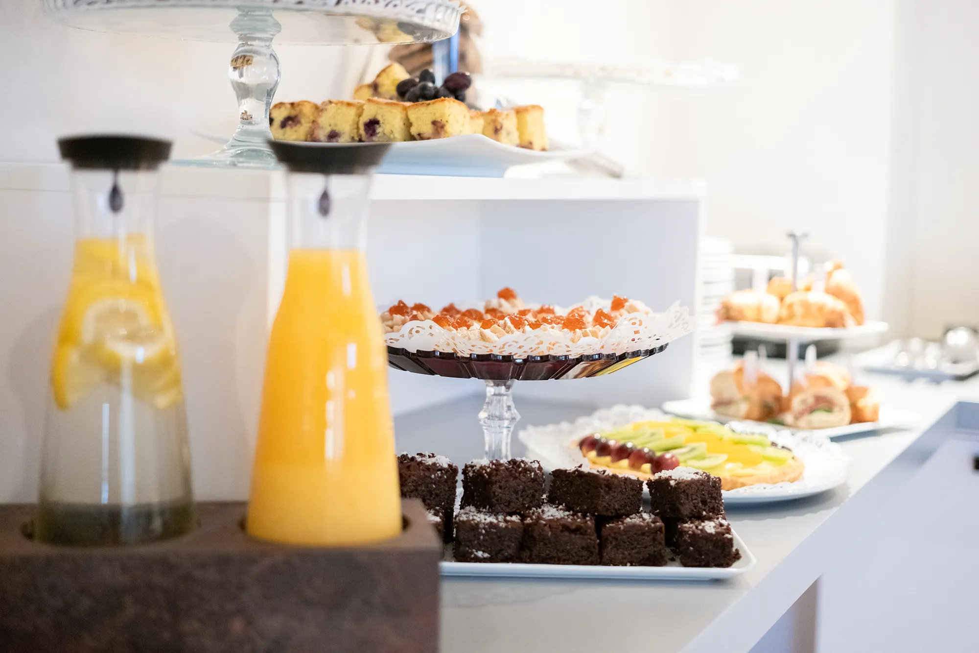 Sweet buffet with juices in glass pitchers, chocolate pastries, fruit tarts, and cakes displayed on stands and trays