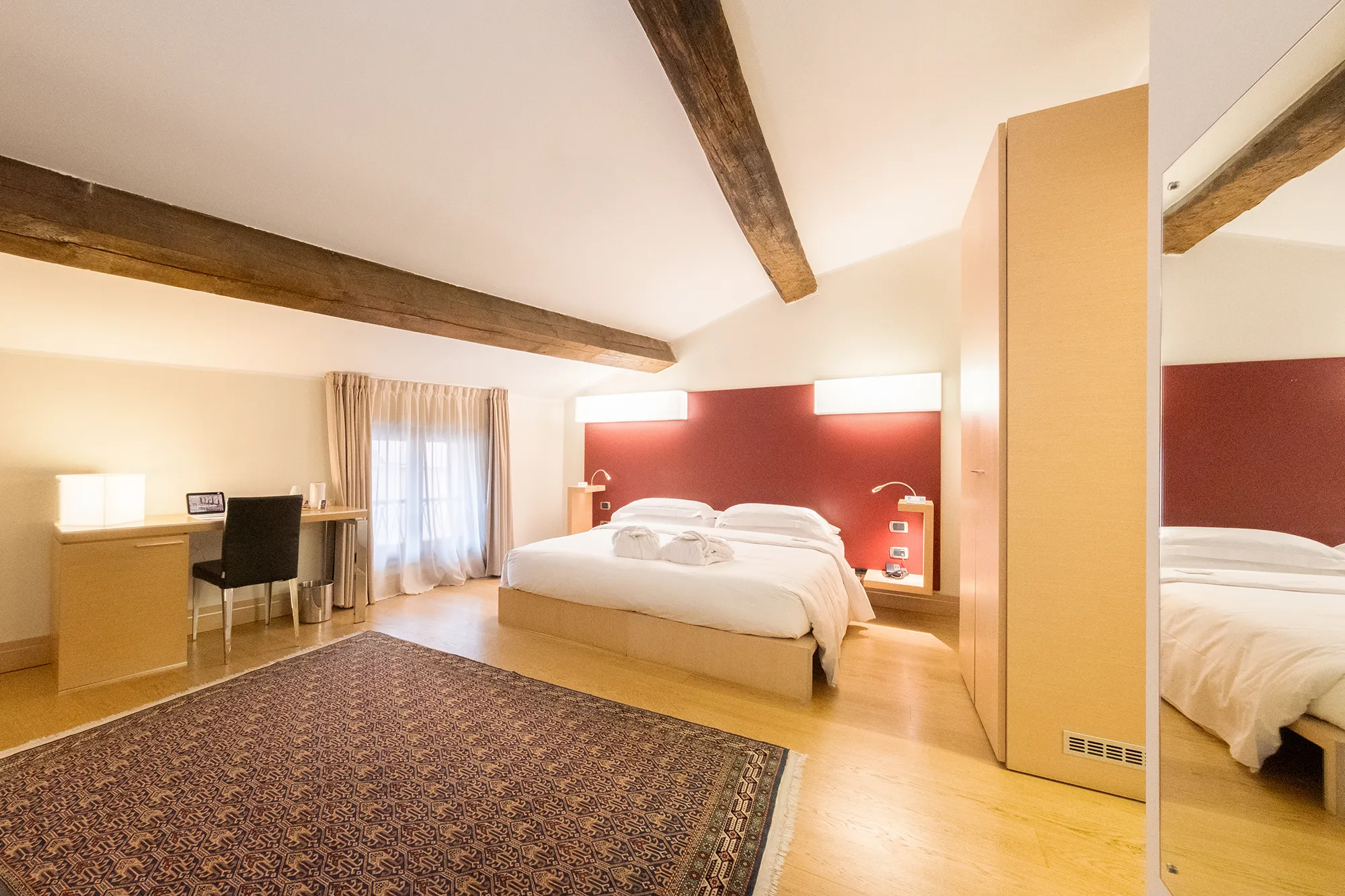 Camera matrimoniale spaziosa con travi a vista, scrivania e luce naturale in hotel a Verona.