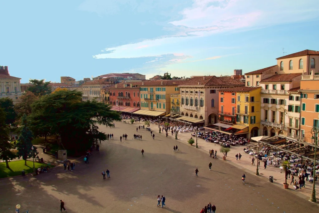 Large urban square with colorful historic buildings, outdoor cafe tables and people strolling under a clear sky